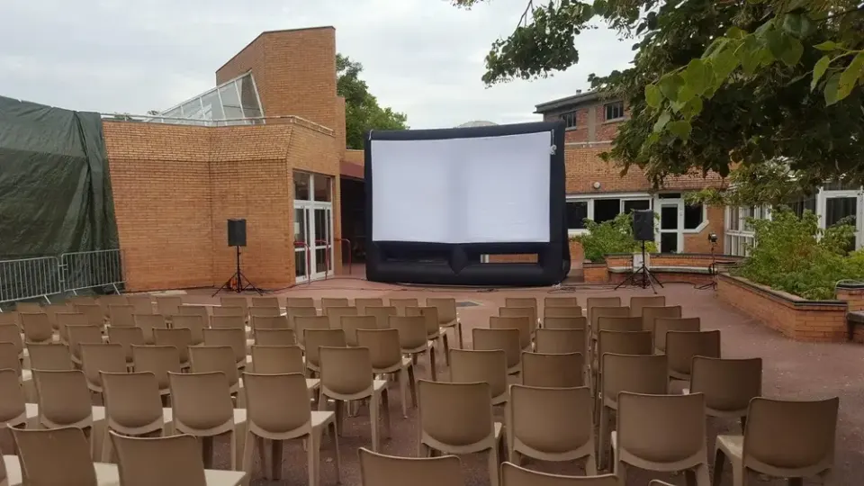Pantalla hinchable económica con soplador en un patio, delante de varias filas de sillas.