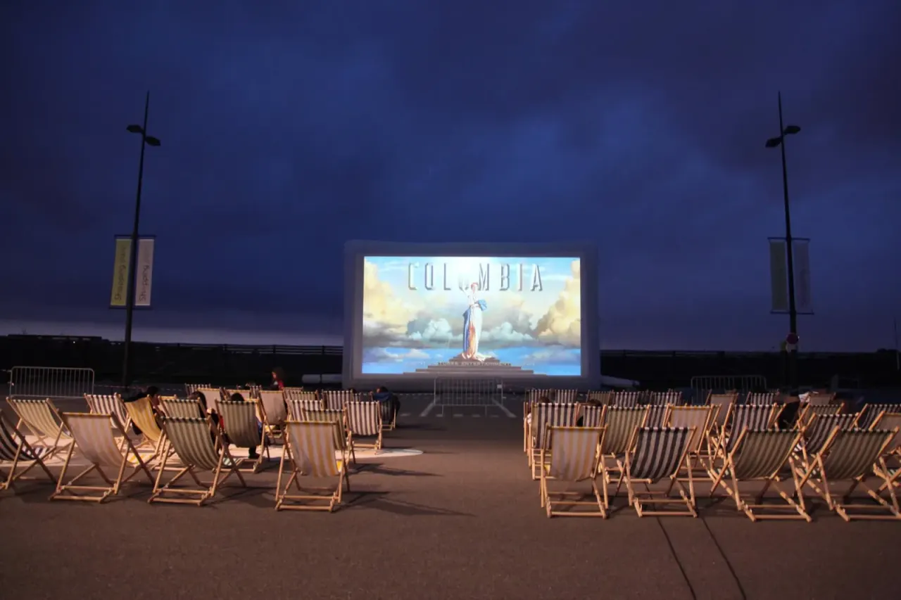 Pantalla de cine hinchable gigante «Hallucine» instalada al aire libre, con tumbonas frente a la pantalla al caer la tarde