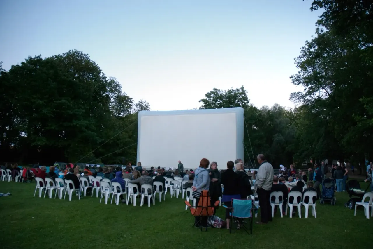 A giant "Hallucine" inflatable movie screen set up in a park, with an audience gathered at dusk