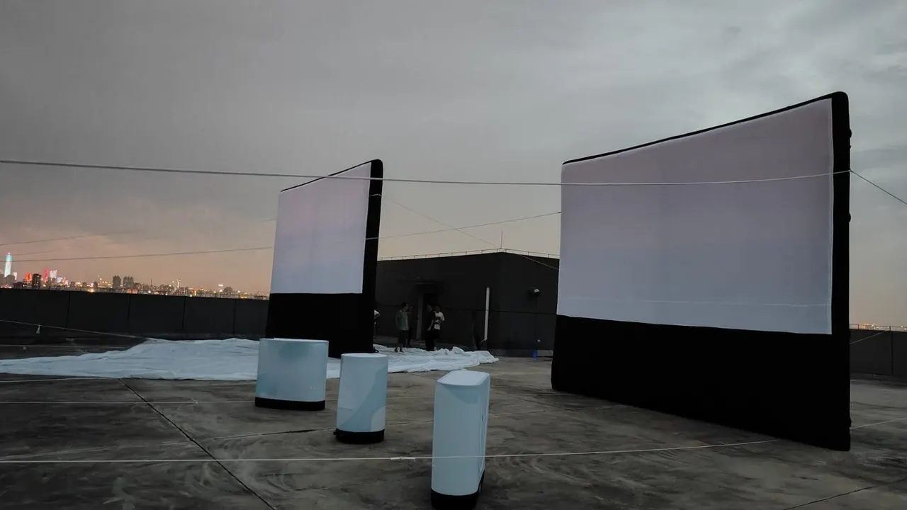 Deux écrans gonflables noirs et blancs installés sur une terrasse de toit avec la skyline urbaine en arrière-plan au crépuscule.